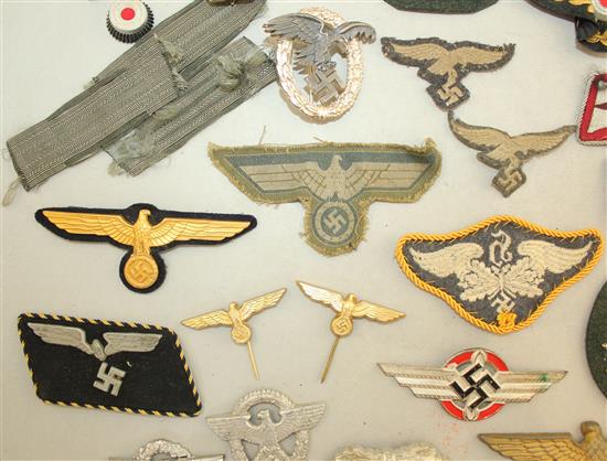 A collection of various German Third Reich cap badges, cloth badges and pins